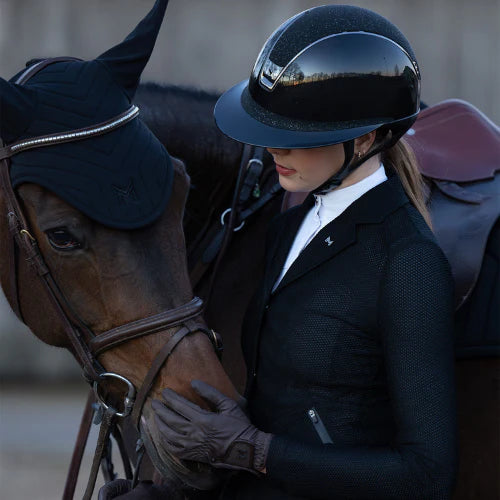 Reiterin streichelt braunes Pferd mit Helm und Turnierkleidung, Turnier-Etikette: Verhaltensregeln & Ablauf eines Reitturniers.