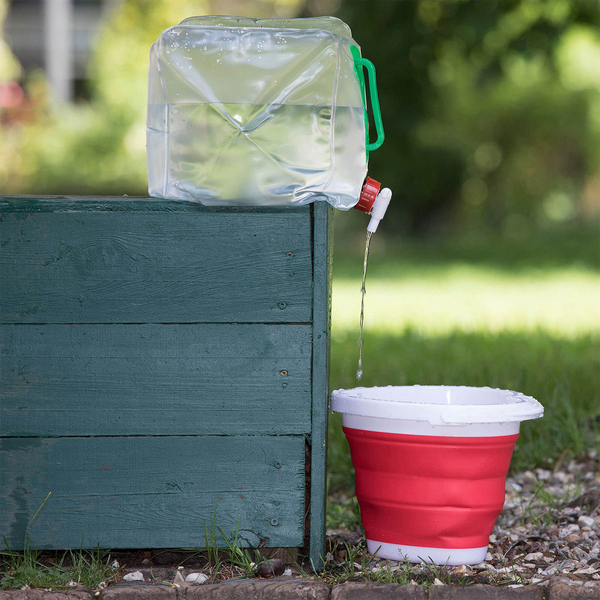 Waldhausen Wasserkanister faltbar 10L, transparent mit grünem Griff, beim Befüllen über einem Becher.