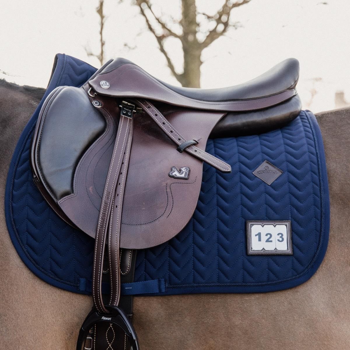 Kentucky Horsewear Springschabracke Fishbone Competition Sattelunterlage, Midsummer Blue, mit Sattel und Startnummer am Pferd.