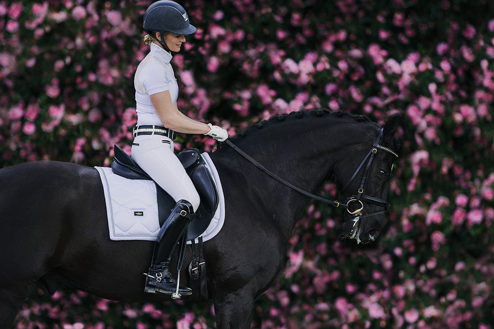 Equestrian Stockholm Dressurschabracke White Perfection Silver, weiß, Reiterin auf schwarzem Pferd in der Reitbahn.