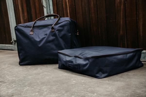 Kentucky Horsewear Schabrackentasche, navy, zwei Taschen auf dem Boden vor einer Stallwand.