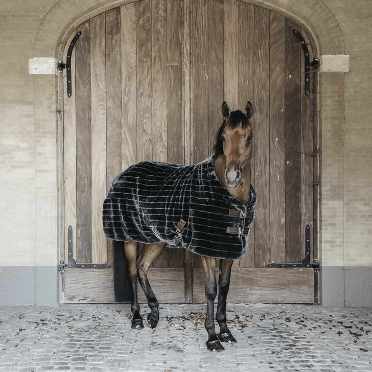 Kentucky Horsewear Stalldecke Fake Fur, Grau, Pferd vor Holztür im Stall.