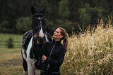 Frau steht neben gesatteltem schwarz-weißem Pferd auf der Wiese, Equines Cushing-Syndrom (ECS) – Ursachen, Symptome und Behandlung