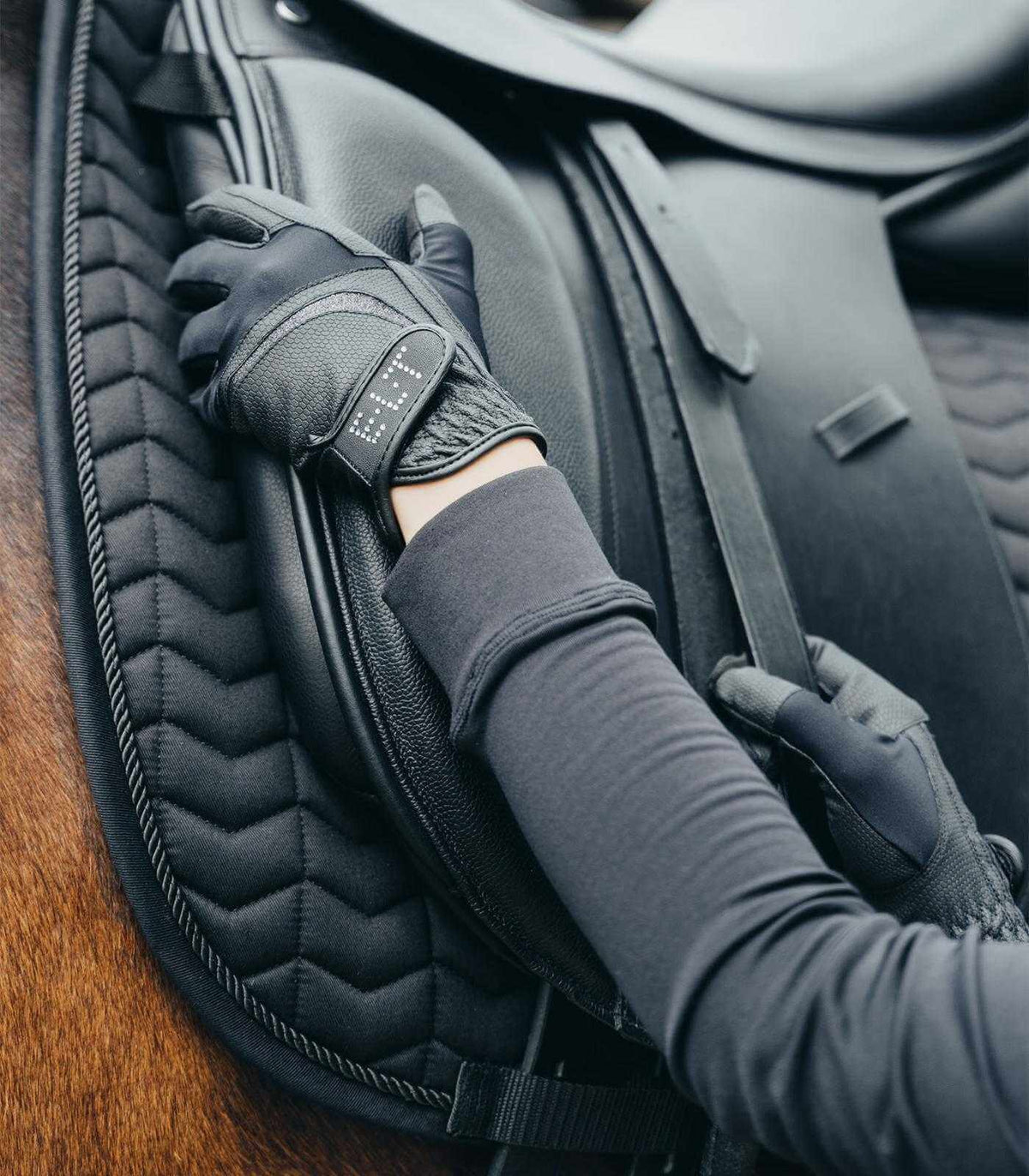 Reithandschuh Noelle, Schwarz, Detailaufnahme am Reitsattel mit Reiterhand.