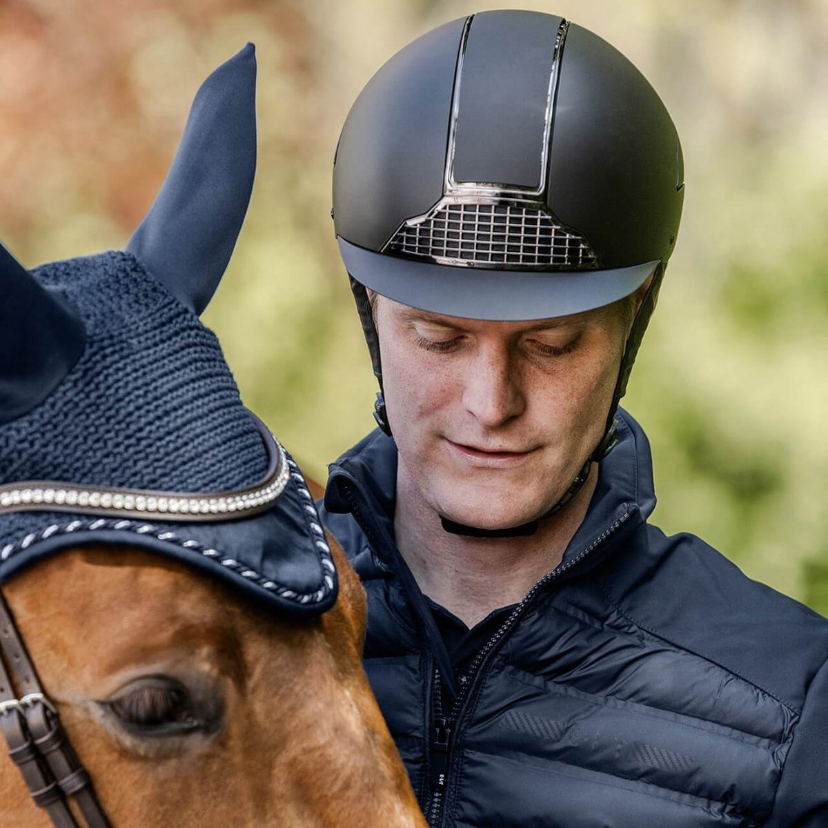 Reithelm Unisex H24 Chrome, Reiter mit Helm neben Pferd.