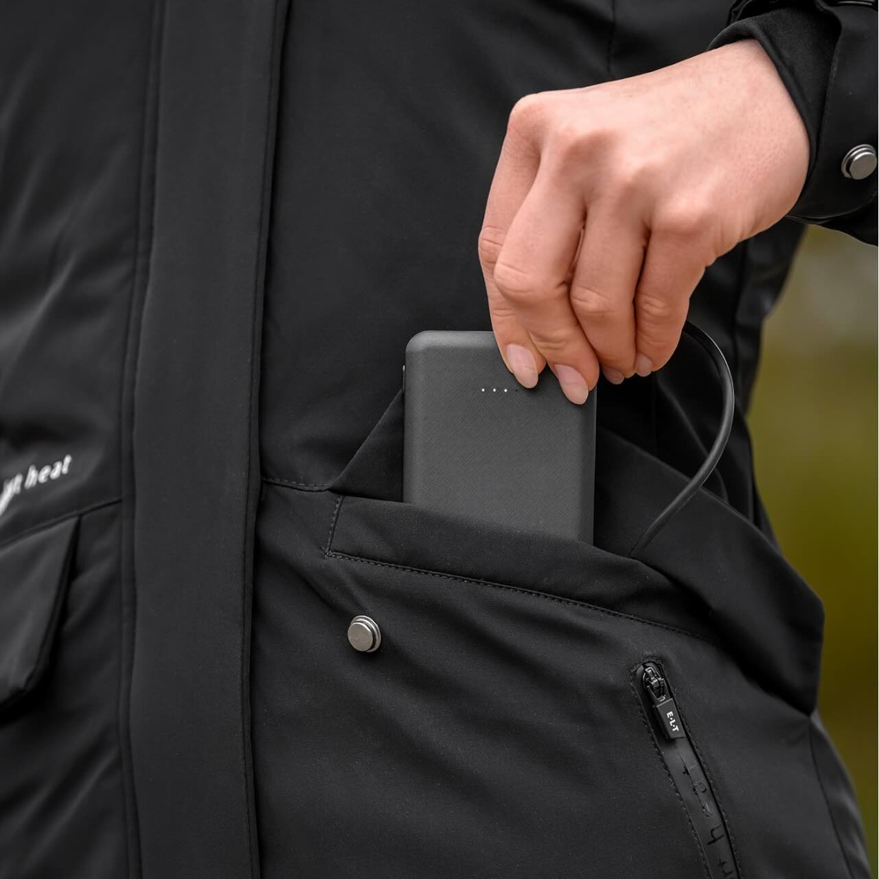 E.L.T Heizparka Damen Comfort Heat Heizjacke, Schwarz, Detailaufnahme einer Person mit Powerbank in der Tasche.