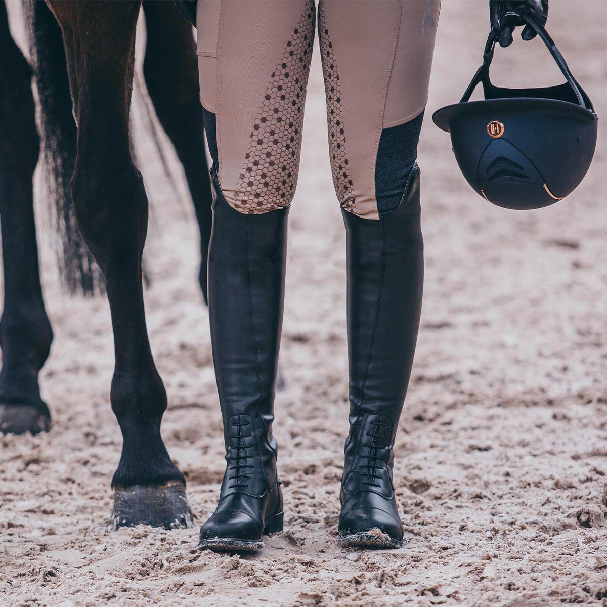 Reitstiefel Nova Tall Vegan, Schwarz, an Reiterin neben Pferd im Reitplatz.