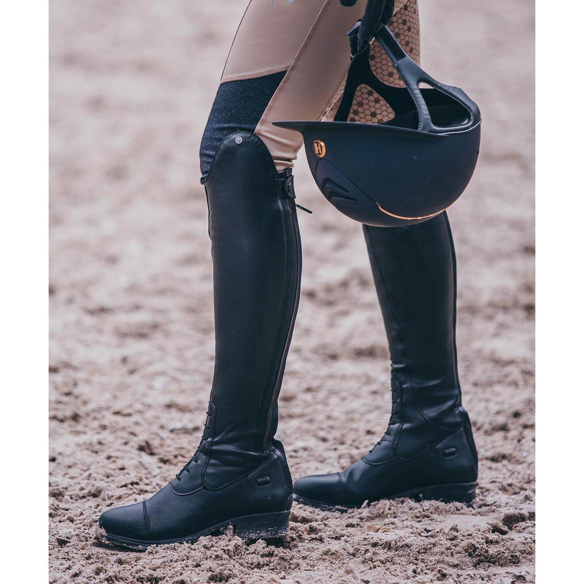 Suedwind Equestrian Reitstiefel Nova Tall Vegan, Schwarz, an einer Person mit Reithelm im Sand.